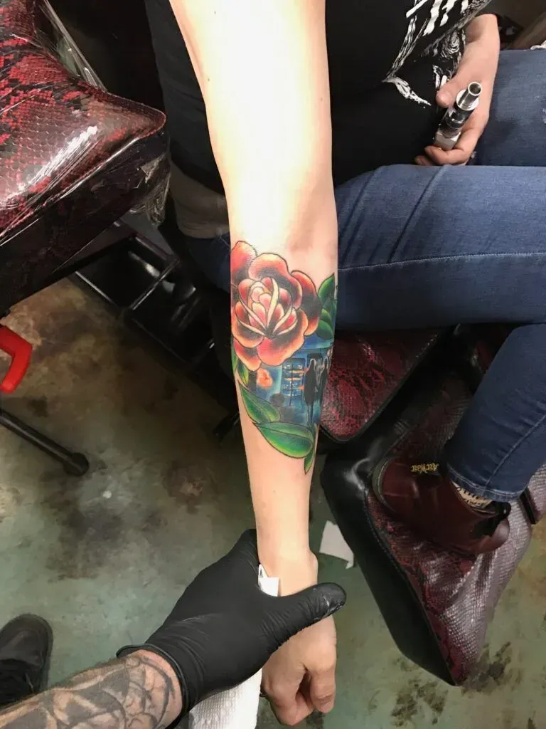 Rose tattoo on an arm, being touched by a gloved hand. The person sits in a tattoo studio.
