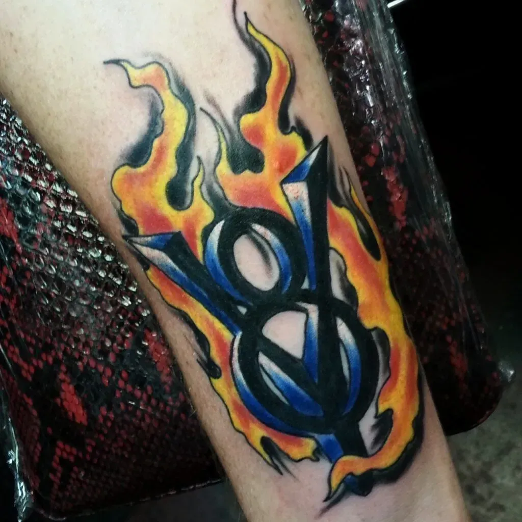 Tattoo of a V8 logo engulfed in flames, on a person's arm. The logo is blue and black with yellow and orange flames.