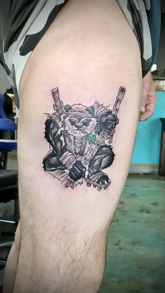 Tattoo on thigh: Ninja panda with swords. Black and gray shading with teal highlights.