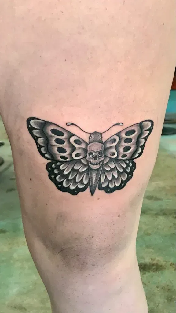 Tattoo of a black and gray butterfly with a skull head, on a leg.