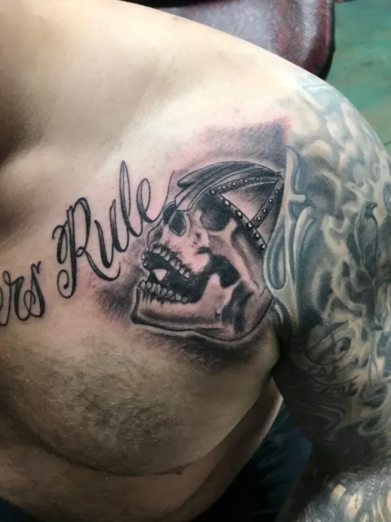 Tattoo on chest: skull wearing headwear with the words