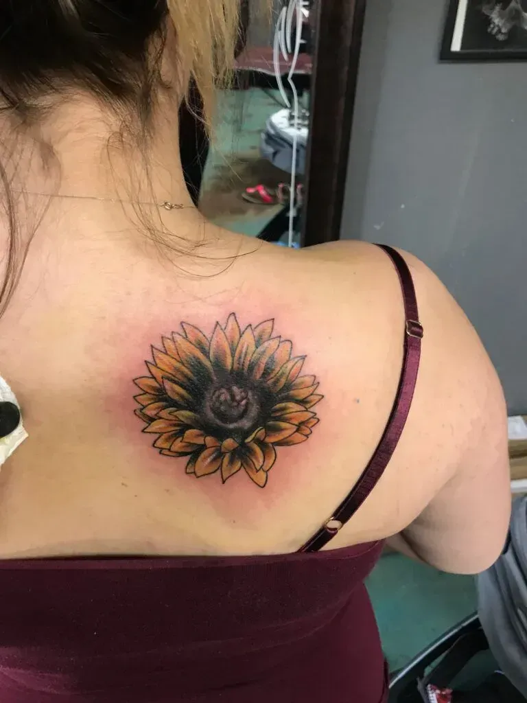 Sunflower tattoo on a person's upper back, in a studio setting. Yellow and black ink.