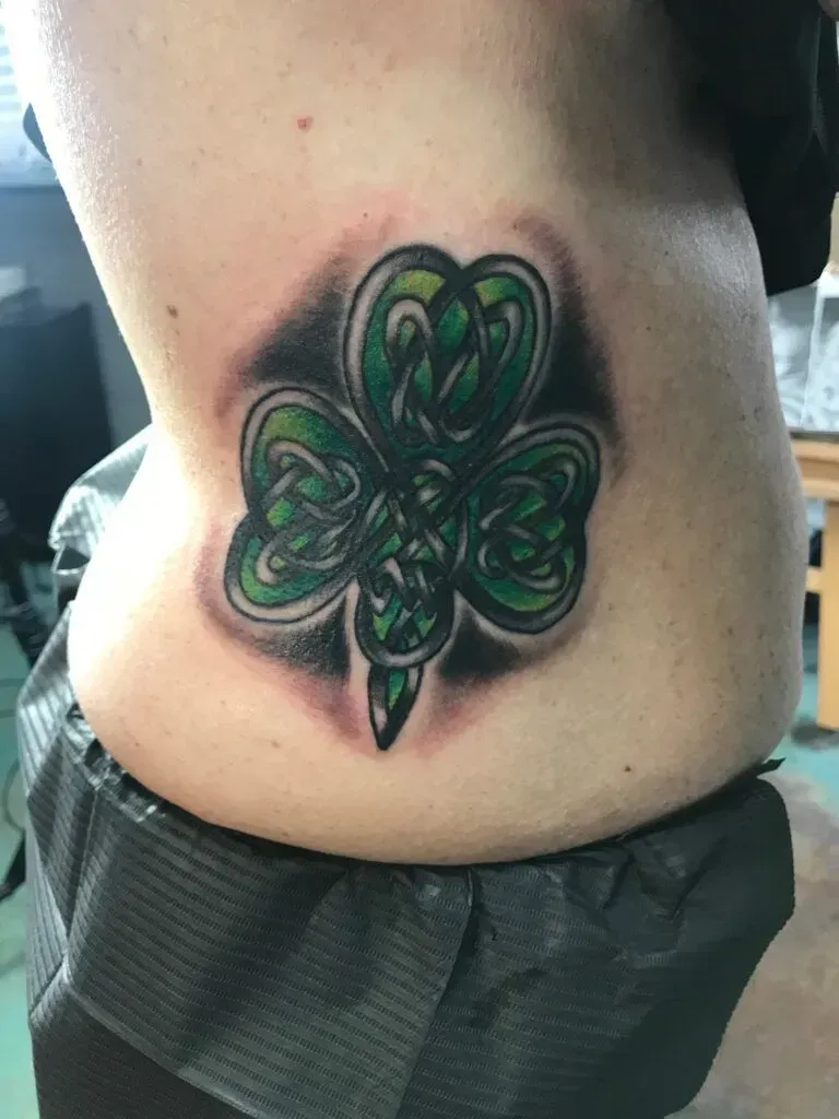 Celtic shamrock tattoo on a person's side, shaded with green, black, and gray.