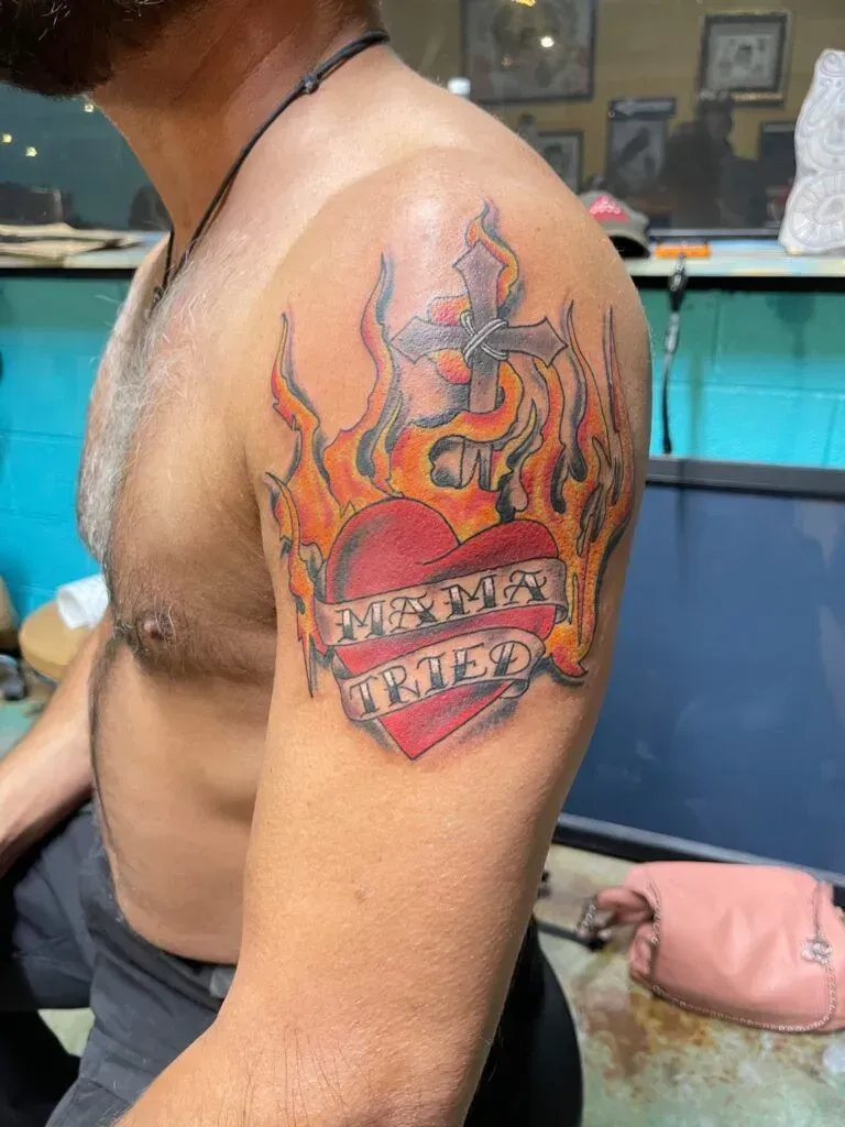 Tattoo of a heart on fire with a banner reading