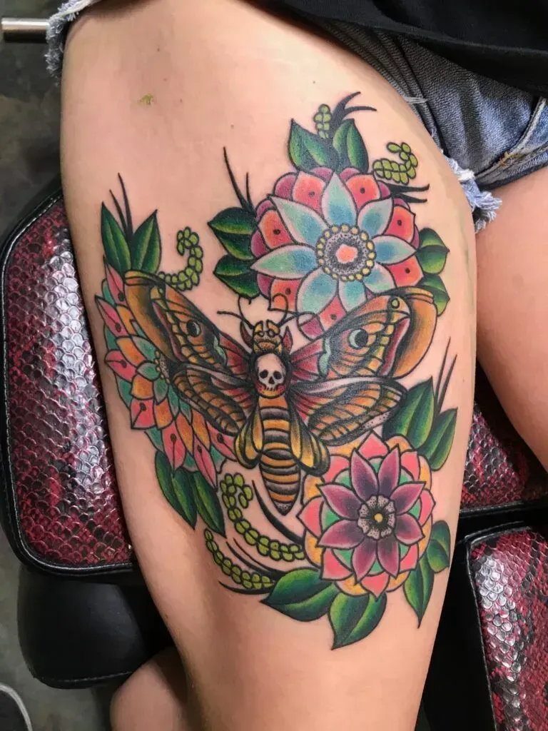 Thigh tattoo with moth and flowers, colorful, traditional style.
