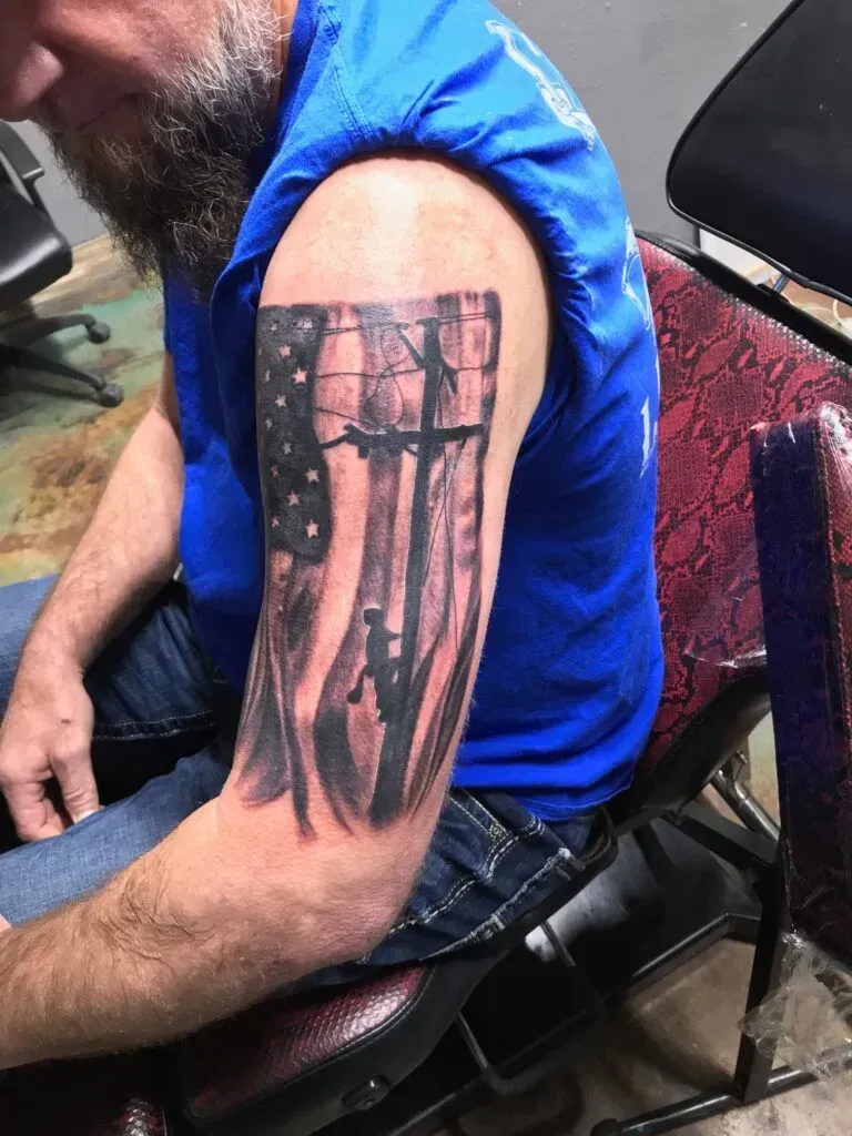 Man with a tattoo of a tattered American flag with silhouettes of soldiers on his upper arm.