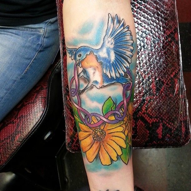 A woman has a tattoo of a bird and flowers on her arm