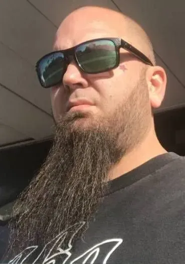Man with sunglasses and long beard, looking slightly down.