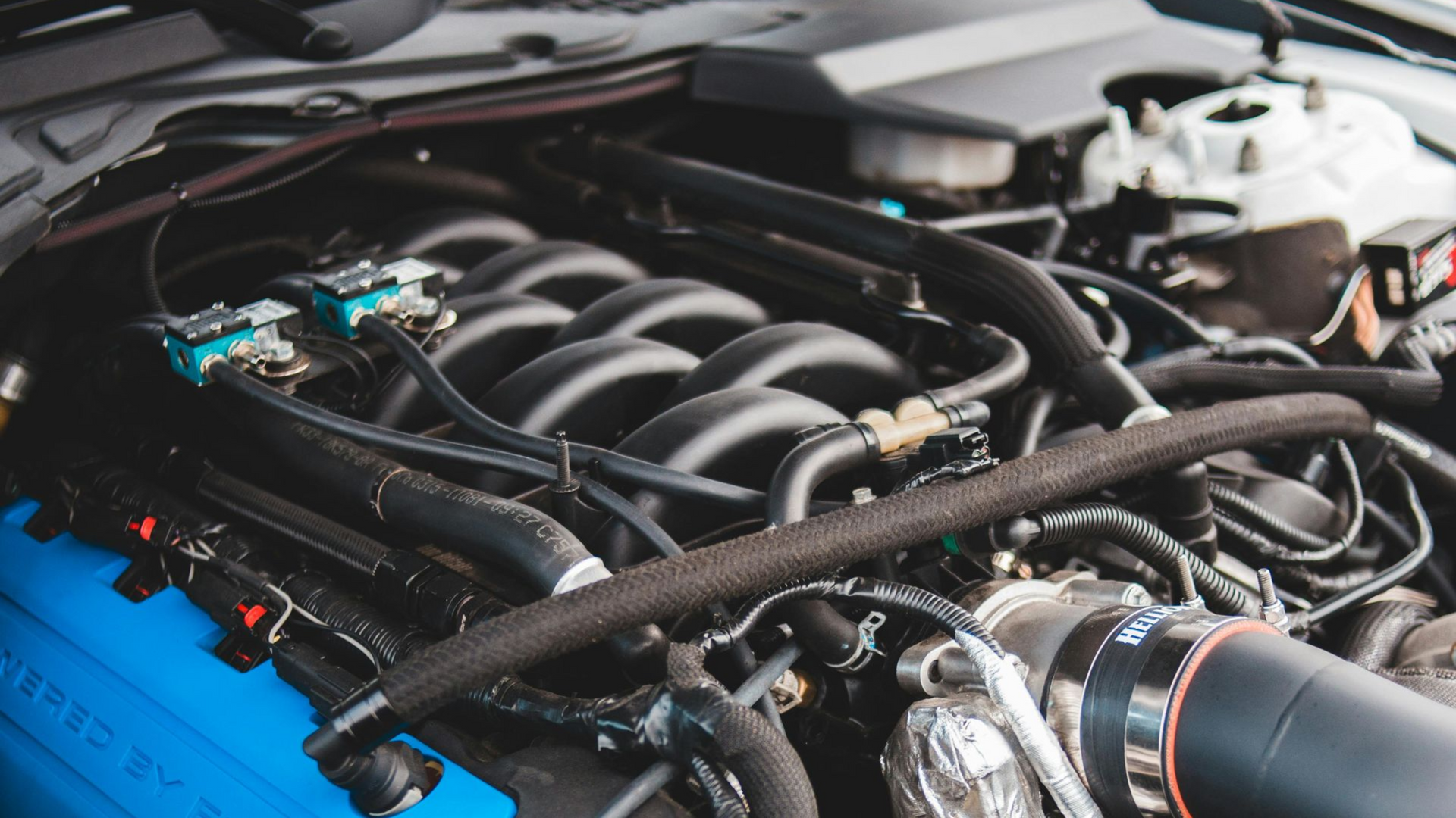 A close-up view of a high-performance car engine with a blue valve cover and black intake manifold components.