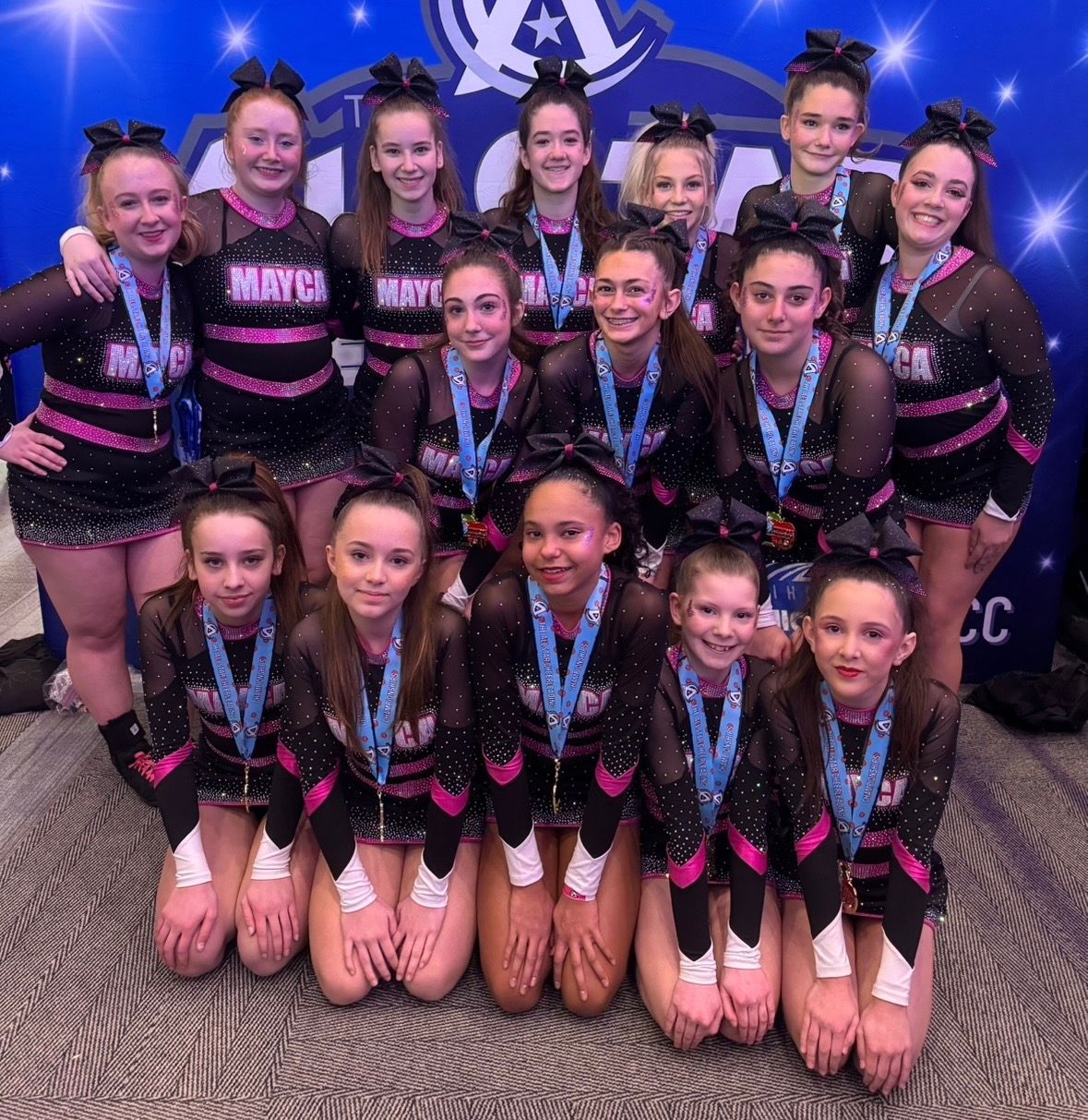 Cheerleading squad in matching black and pink uniforms, posing with medals at an event.