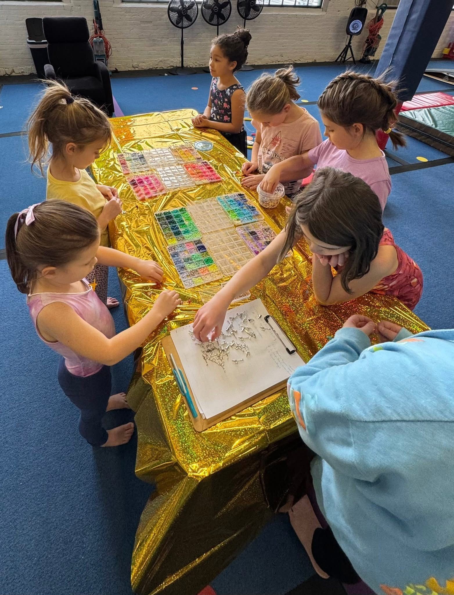Children around a table covered in gold cloth, working on projects.