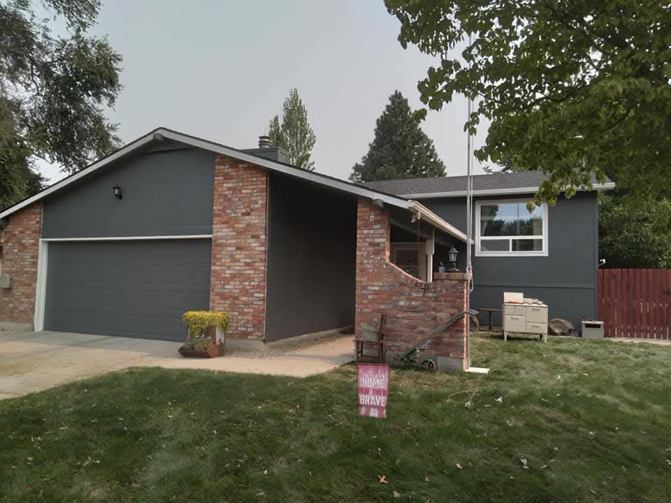 Exterior paint job of a house with gray siding and a red brick wall