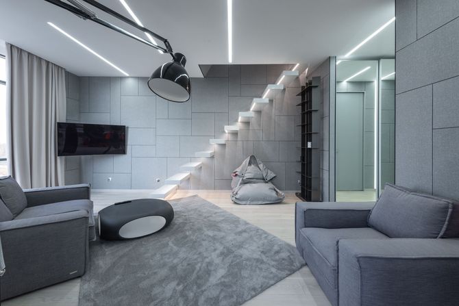 Modern gray living room with sectional sofas, staircase, and hanging lamp in a sleek contemporary interior