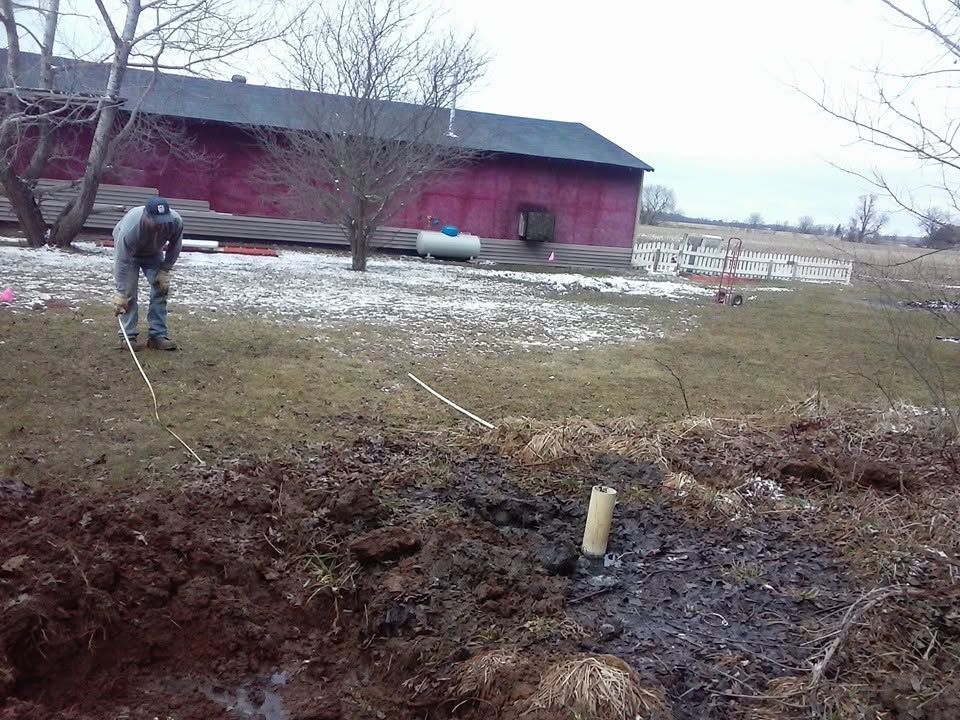 Person spraying a red barn in a snowy field with a hose or pressure washer
