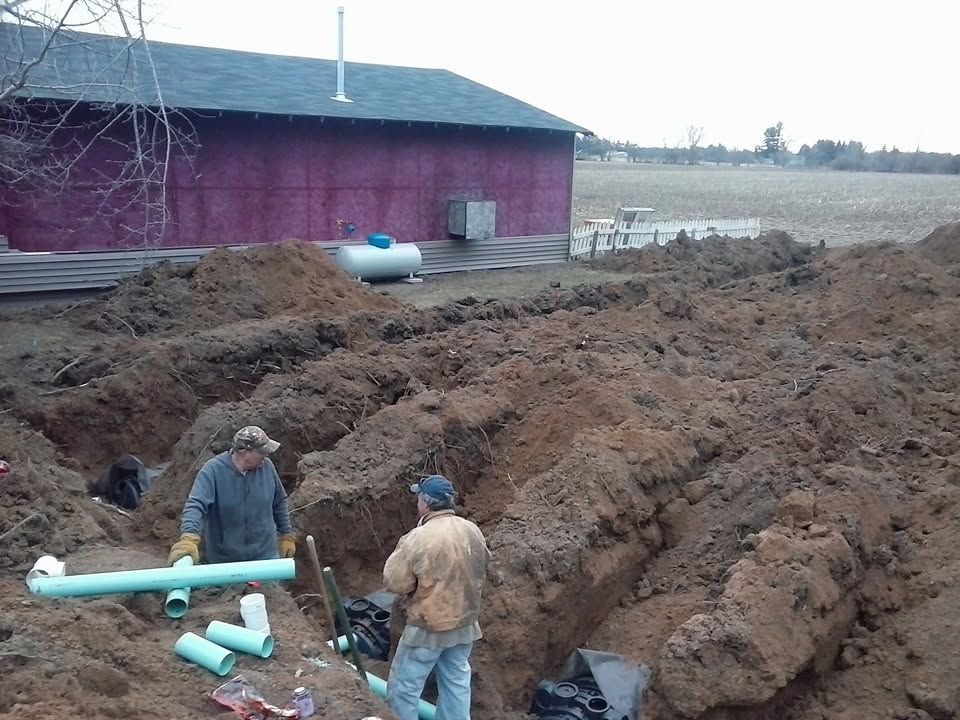 Workers installing green pipes beside a red barn in a muddy excavation area
