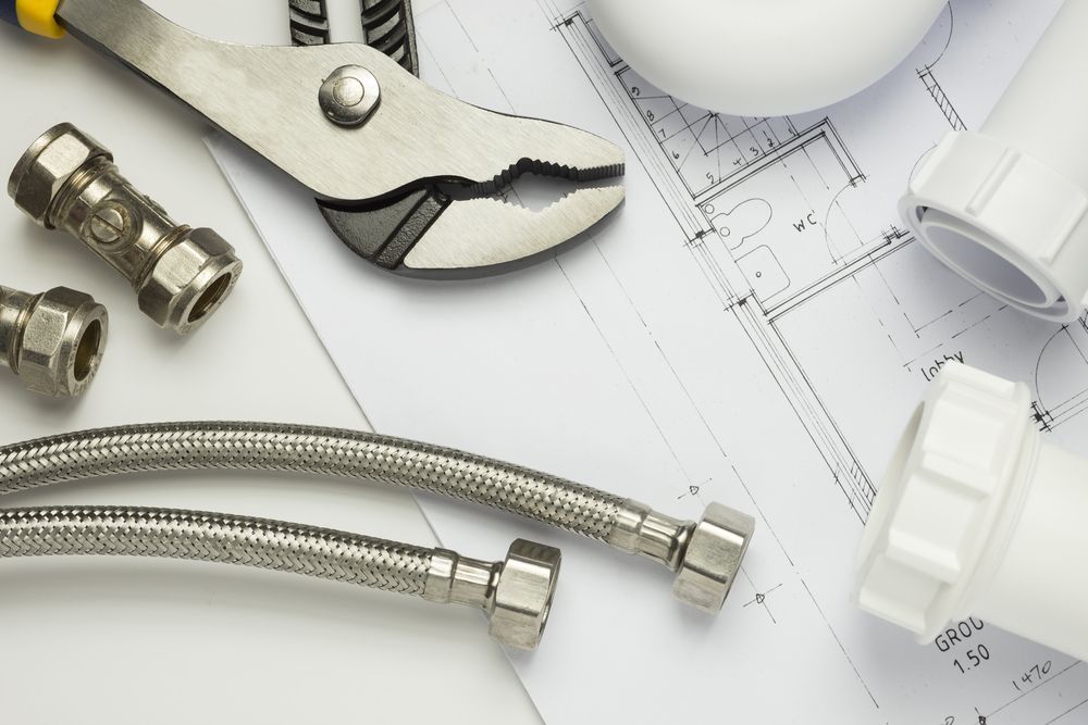 Plumbing tools, metal hoses, and white plastic pipes arranged on top of a technical blueprint— GPE Plumbers In Kendall, NSW