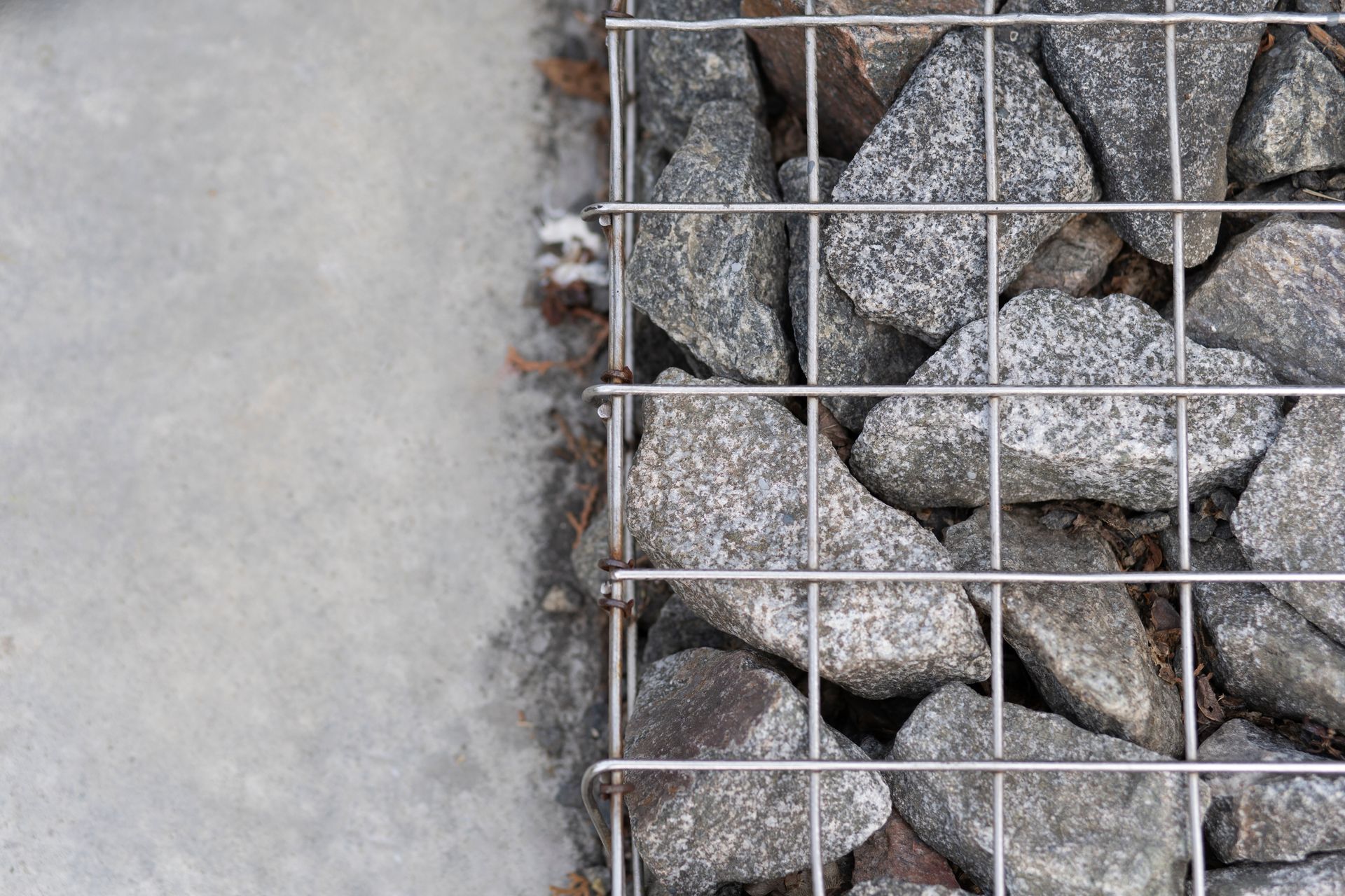 A Close-Up View of Grey Stones Packed Inside a Wire Mesh Cage, Positioned Next to A Smooth Concrete Surface — GPE Plumbers In Kendall, NSW