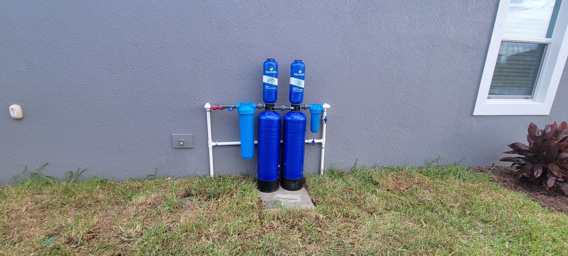 Two blue water filters are sitting in the grass in front of a house.