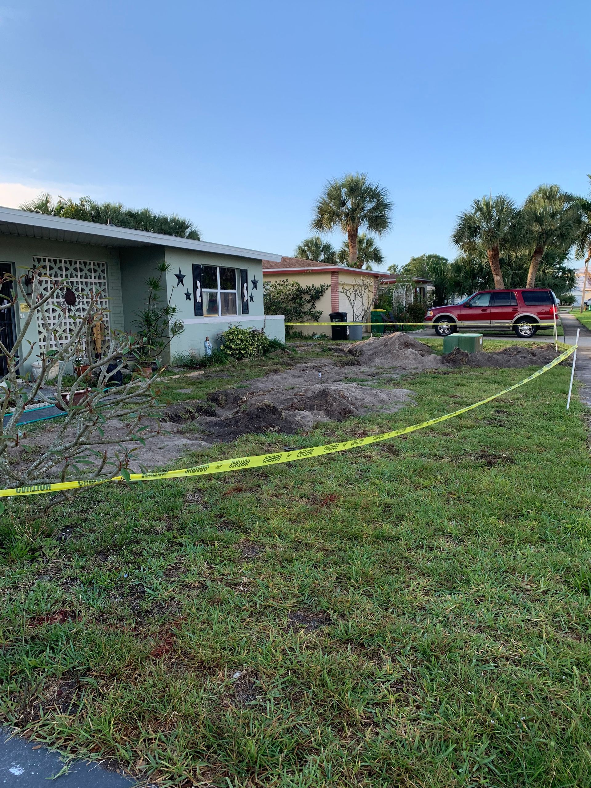 A house with a red suv parked in front of it is surrounded by yellow tape.