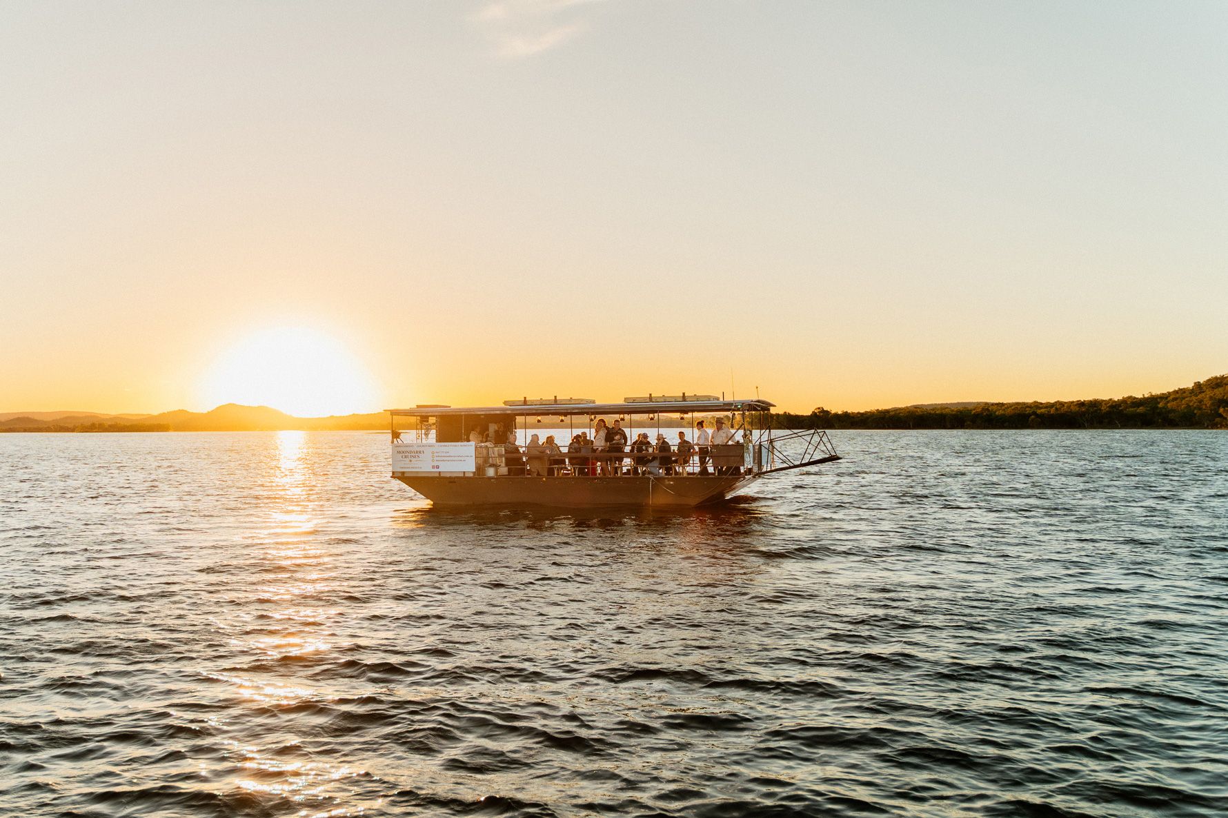 Boat on water at sunset, with the sun low on the horizon and a warm orange sky.