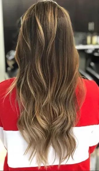 Long, wavy brown hair with blonde balayage highlights, viewed from behind. The person wears a red and white top.