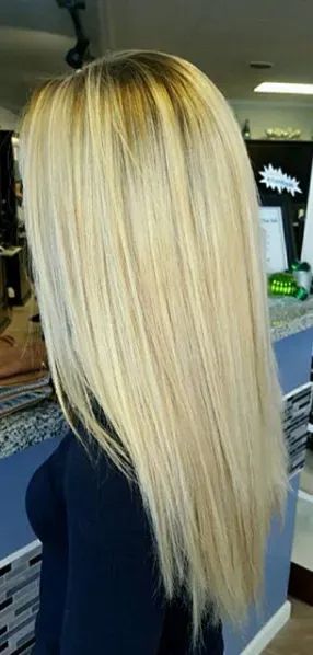A close-up view of long, straight, blonde hair with dark roots, styled in a salon setting.