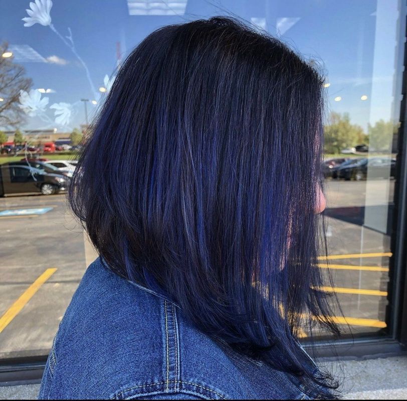 A person with a dark, shoulder-length angled bob hairstyle featuring subtle blue highlights, viewed from the side.