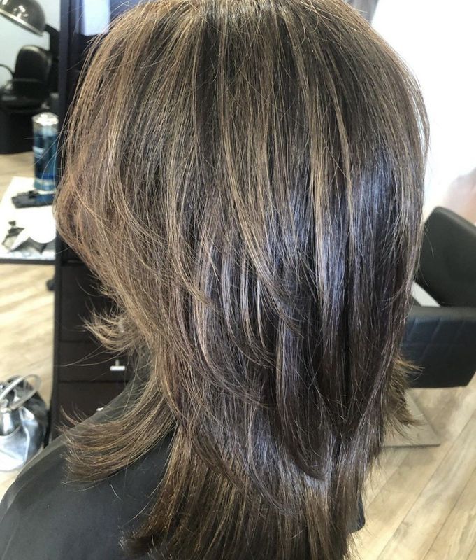 Back view of shoulder-length, dark brown hair with layered, feathered styling in a salon setting.