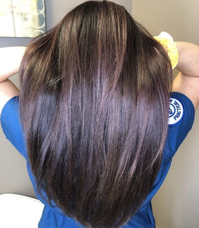 A person with long, straight, dark brown hair with subtle purple undertones, seen from behind wearing a blue scrub top.