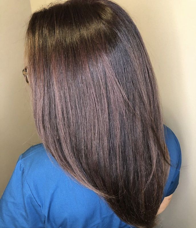 A person with long, straight, dark brown hair with subtle purple undertones, seen from behind wearing a blue top.