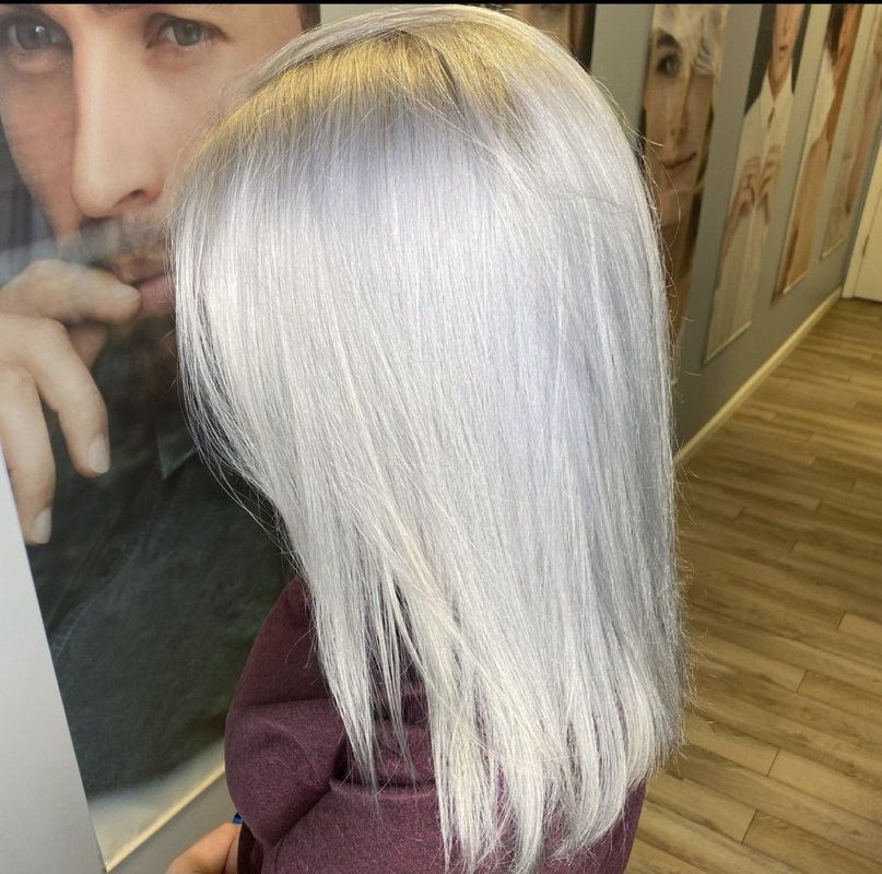A person with shoulder-length, straight hair colored a bright, icy silver-white, seen from behind in a salon setting.