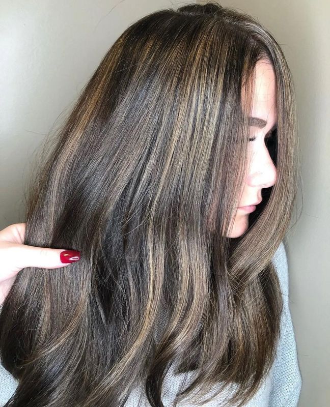 A person with wavy, brown hair featuring lighter caramel-colored highlights.