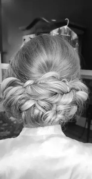 A close-up of a person with blonde hair styled in an elegant, intricate low braided updo, viewed from behind.