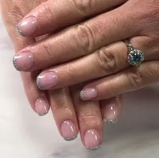 A close-up of hands showing a French manicure with silver glitter tips, wearing a ring with a blue stone.