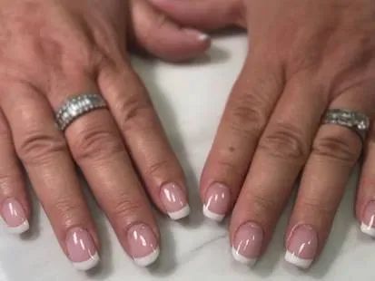 Two hands with a French manicure, featuring pink nail beds and white tips, with diamond bands on both ring fingers.
