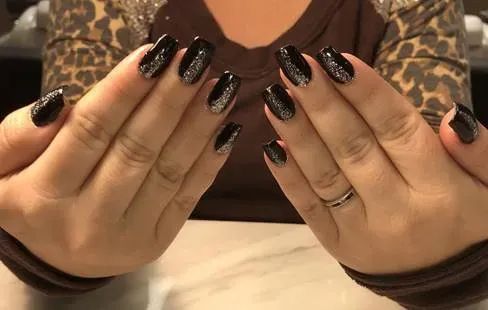 Hands displayed with black manicured nails featuring a vertical silver glitter stripe on each nail.