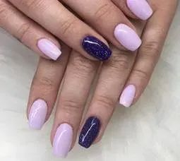 A close-up of hands with manicured nails, alternating between light lavender and deep purple glitter polish.