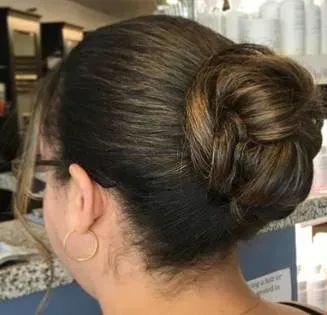 A person with dark brown hair styled in a neat, braided bun, shown from the side with a small loose strand near the ear.