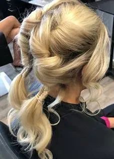A back view of blonde hair styled in two loose, twisted low ponytails with wavy, voluminous sections at the crown.