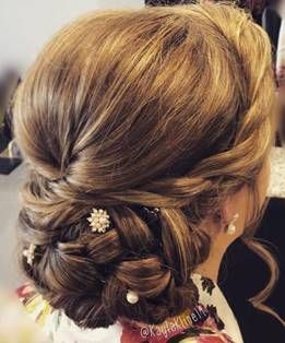 A close-up view of an intricate, braided low updo hairstyle with brown highlights, adorned with small pearl hairpins.