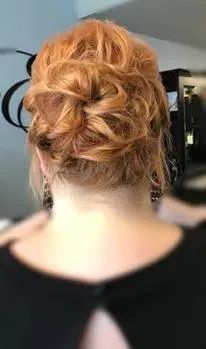 A person with wavy, reddish-blonde hair styled in an elegant, loose updo, viewed from behind.