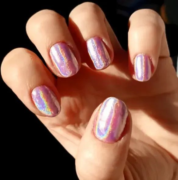 A hand displaying nails with a pearlescent, holographic chrome finish that reflects shades of light pink and purple.