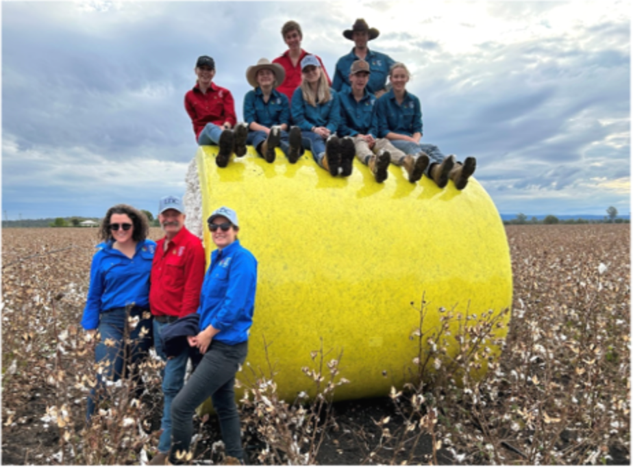 A group of people sitting on top of a large yellow ball in a field