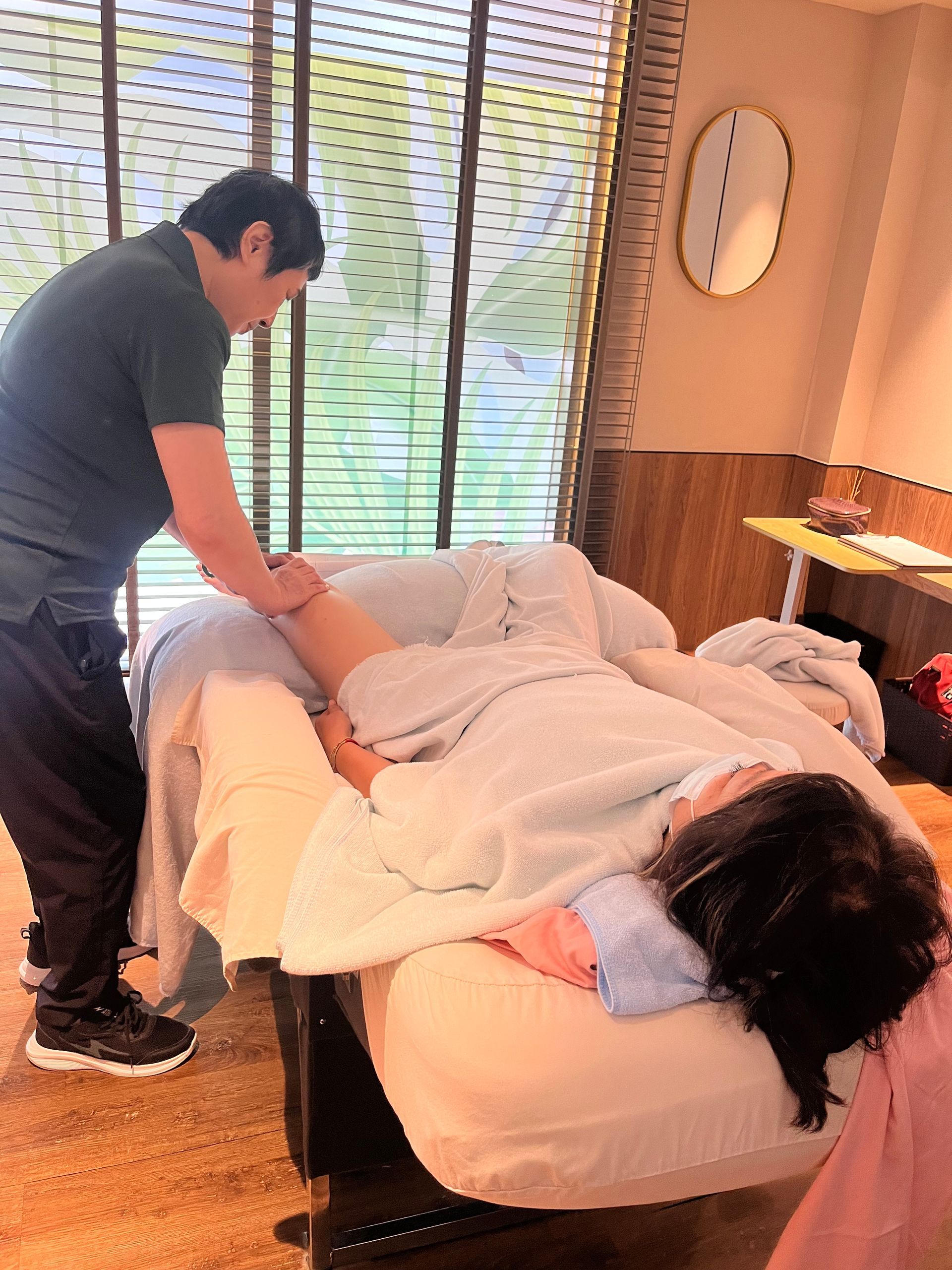 男子在室內為躺在按摩床上的人進行腿部按摩。