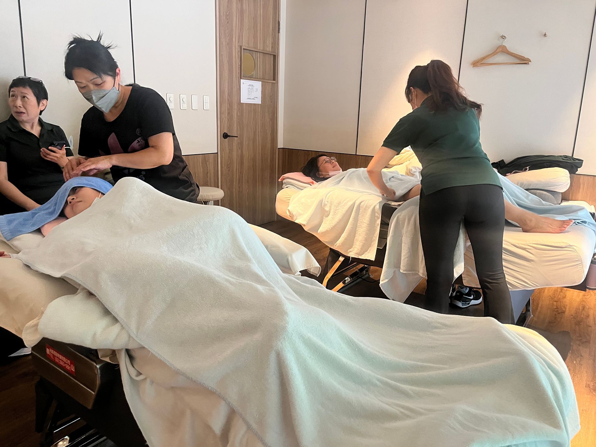 人們躺在按摩床上接受按摩，按摩師正在工作。明亮的室內環境。