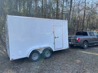 White enclosed cargo trailer hitched to a gray pickup in a wooded area