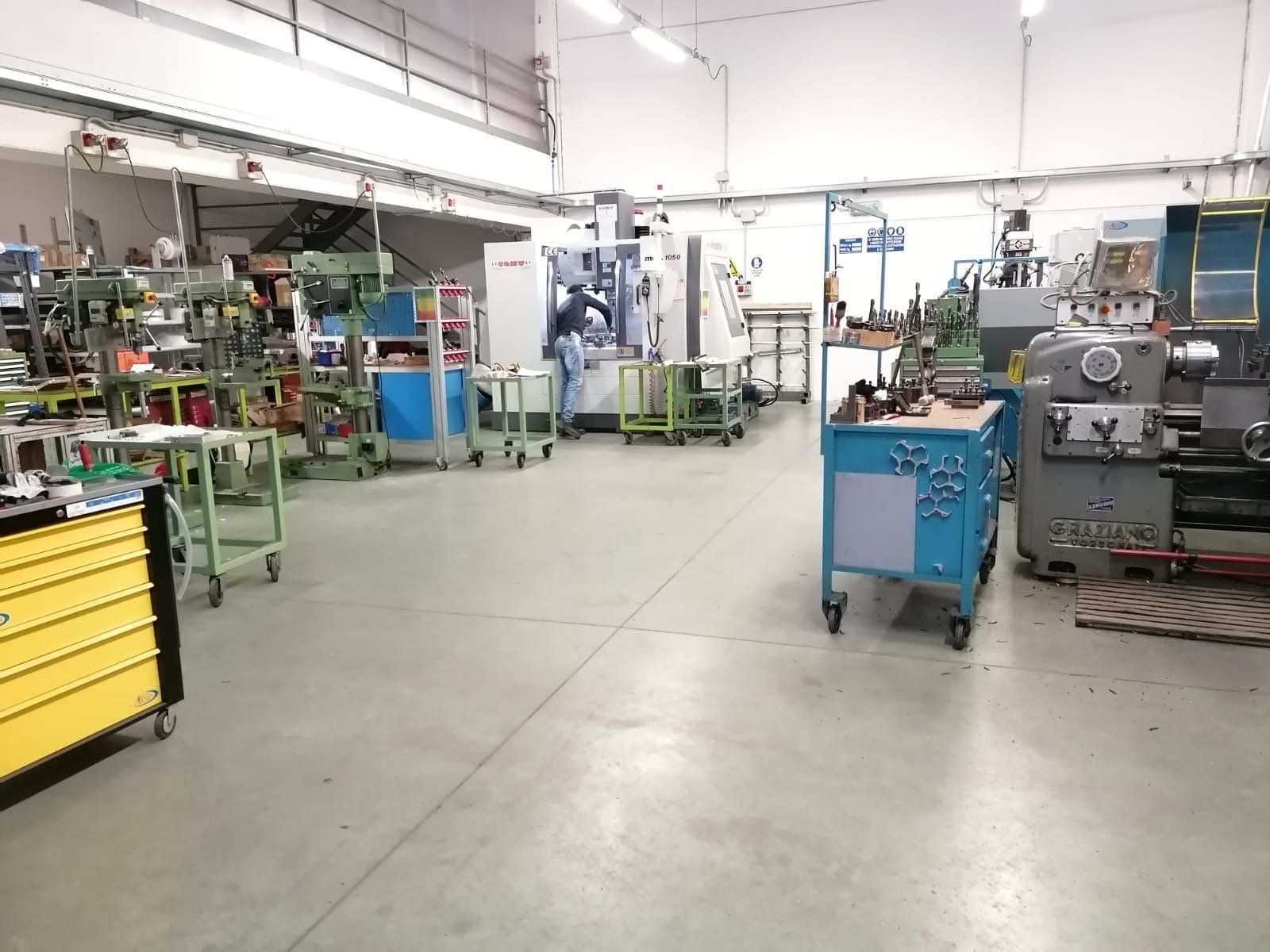 Industrielle Werkstatt mit Maschinen, Werkzeugwagen und Werkbänken in einer hellen, geräumigen Fabrikhalle