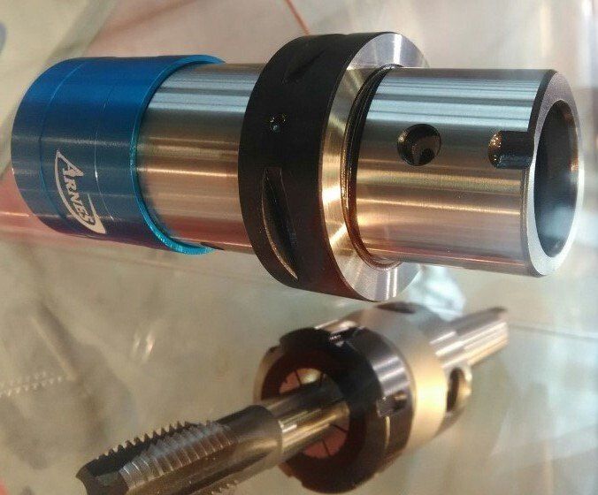 Zwei mechanische Metallteile, ein blau-silbernes zylindrisches Bauteil und ein silbernes Gewindeteil, auf einer weißen Oberfläche
