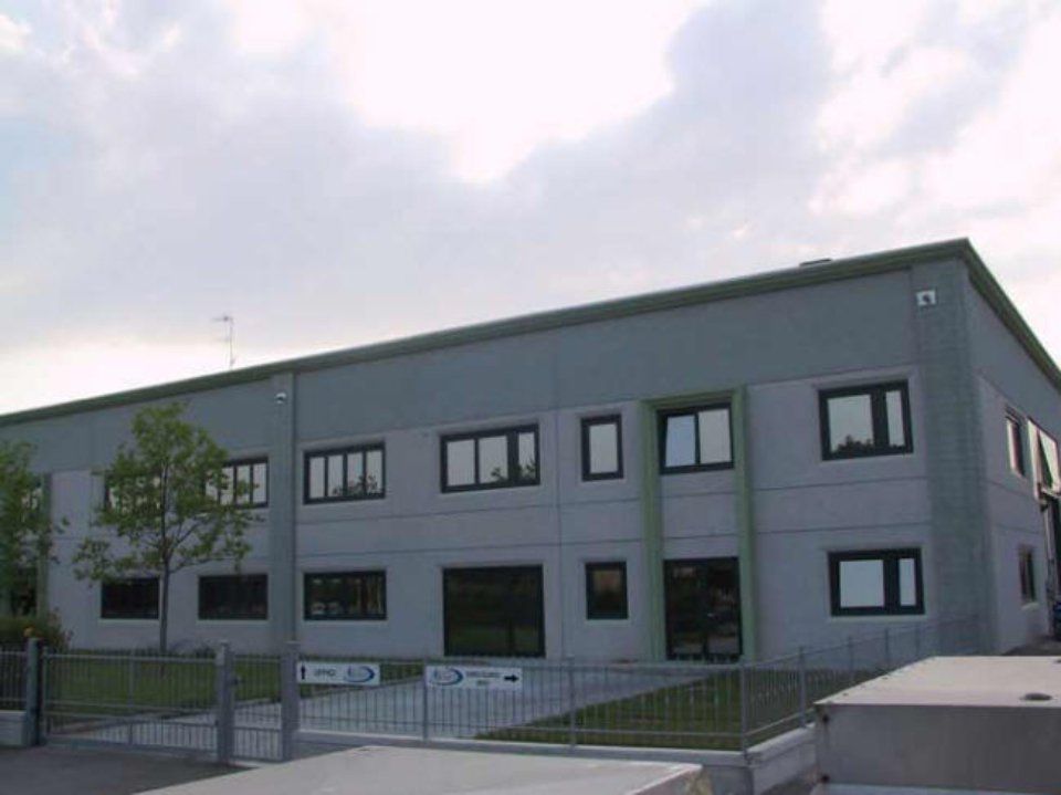 Modernes, graues, zweistöckiges Bürogebäude mit schwarzen Fenstern und einem kleinen, umzäunten Eingang