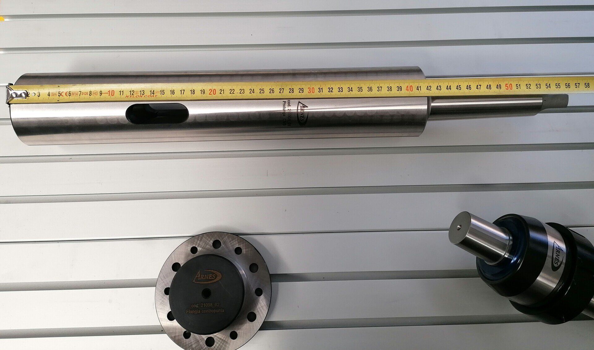 Teile eines Metallbearbeitungswerkzeugs und einer Messuhr sind auf einer linierten Fläche ausgelegt, darüber befindet sich ein Lineal.
